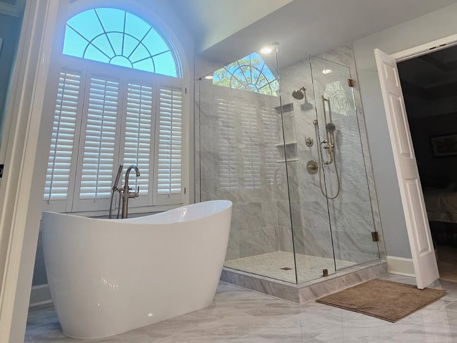 Remodeled primary bathroom with a freestanding soaking tub, frameless glass shower with marble-look tile, and a large-format tile floor