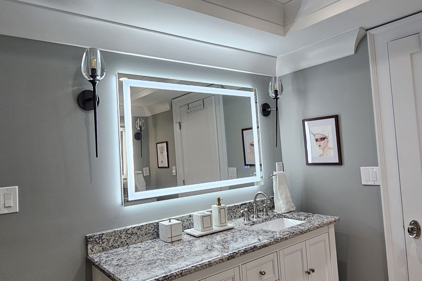 Bathroom vanity with a stone countertop, backlit mirror and wood-look tile flooring