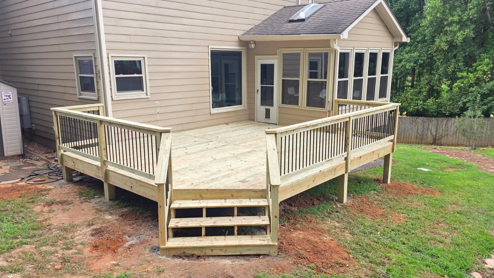 New pressure-treated wood deck with black metal balusters and steps down to the lawn, built onto the back of a tan-sided house