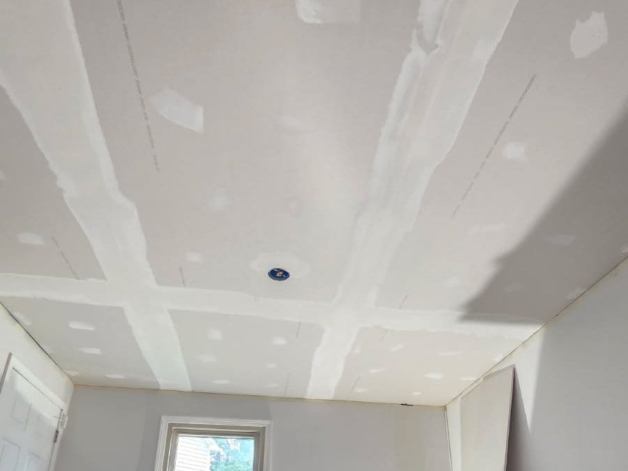 New drywall ceiling hung and taped, with seams and screw holes mudded ahead of sanding
