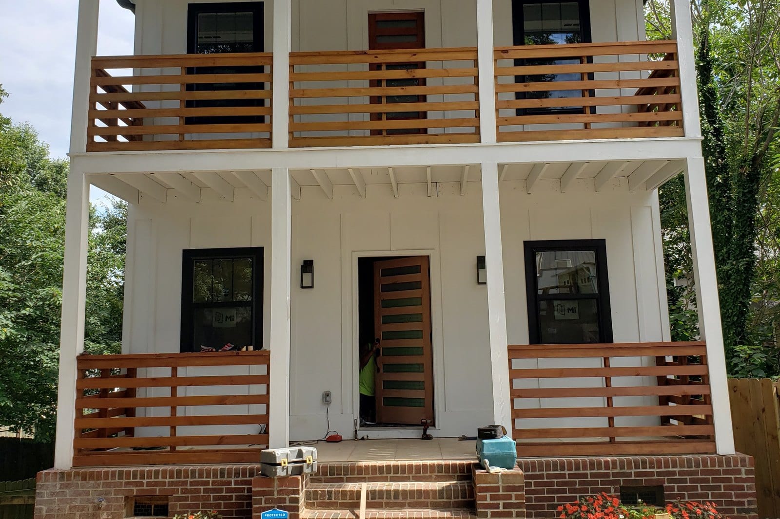 Two-storey home exterior painted white with a horizontal slat balcony rail and a brick foundation