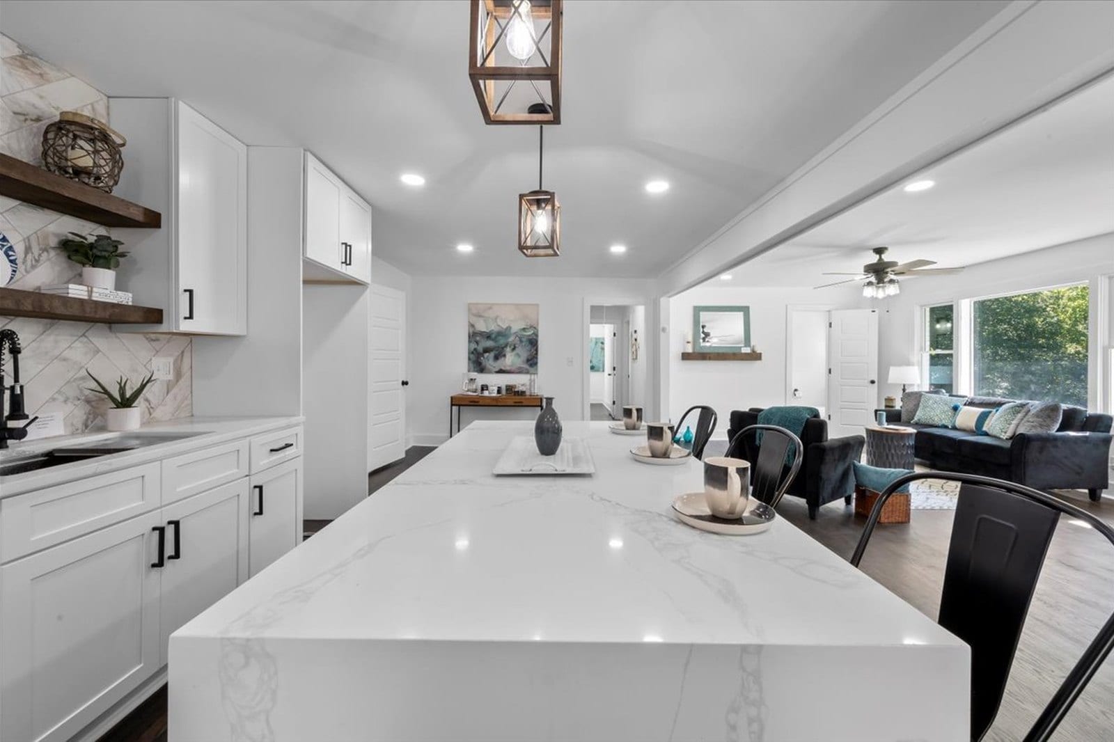 Open-plan kitchen and living space with a white quartz waterfall island, pendant lighting and an open shelf